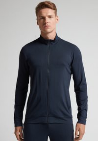 Chaqueta zip-up azul marino hecha de tela suave y ligera. Presenta un cuello alto, mangas largas y un diseño ajustado para un aspecto aerodinámico.