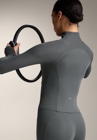 Grå randig långärmad tränings tröja med hög krage, tillsammans med svarta träningsredskap, som framhäver en figurnära silhuett och smidig textur.