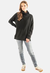 Suéter de punto negro de gran tamaño con escote de tubo, puños acanalados, combinado con jeans de color azul claro y zapatillas beiges con acentos en burdeos.