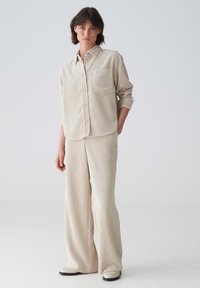 Beige vertical-striped shirt with a pocket, paired with matching wide-legged pants. Both feature a soft texture and relaxed fit.