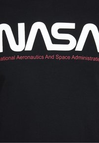 Camiseta de algodón negra con gran texto en blanco "NASA" y debajo en maroon el texto más pequeño "Administración Nacional de Aeronáutica y del Espacio". Textura suave.
