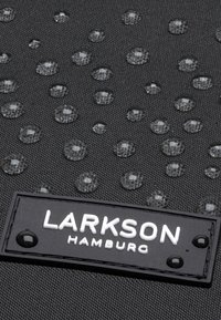 Černý materiál s texturovaným povrchem, na němž se nacházejí jasné kapky vody. Na obdélníkové černé etiketě je bíle napsáno "LARKSON HAMBURG".