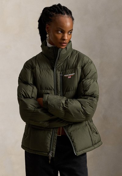 Alyvų žalios spalvos pūkinė striukė su aukštu apykakle, užtrauktuku ir logotipu ant krūtinės. Yra siūtinė tekstūra ir šoninės kišenės.