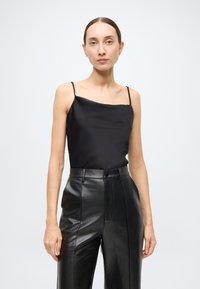 Schwarzes Satincamisole mit dünnen Spaghetti-Trägern, kombiniert mit hoch taillierten schwarzen Lederhosen mit glatter Textur und geradem Bein.