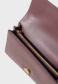 Bolsa de couro malva aberta para mostrar o compartimento principal com fecho de zíper dourado e fecho de clasp dourado na aba da frente, em fundo branco.