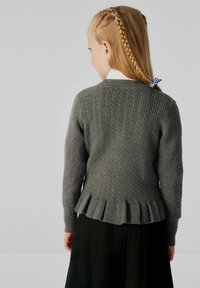 Grauer gestrickter Pullover mit strukturiertem Rippdesign, flared Faltenbesatz am Saum und langen Ärmeln, kombiniert mit einem schwarzen Faltenrock.