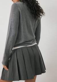 Maglione grigio realizzato in materiale morbido, abbinato a una gonna grigia plissettata. L'outfit presenta una texture sottile e una vita aderente.