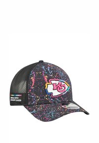 Casquette noire avec motif éclaboussé coloré, arborant un logo blanc avec des accents rouges et bleus. Dos en maille avec une étiquette sur le côté pour sensibiliser au cancer.