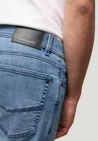 Jean en denim bleu clair avec une étiquette en cuir portant le logo "pierre cardin", cinq poches et des détails de couture au dos.