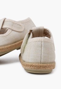 Lichtbeige stoffen schoenen met een gestructureerd oppervlak, elastische band en een tan gevlochten zool. Afgeronde achterkant met een kleine lus voor gemakkelijk aan- en uittrekken.