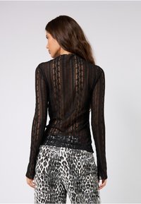 Schwarzes Spitzenoberteil mit langen Ärmeln und gestreiftem Muster. Kombiniert mit gemusterten, eng anliegenden Hosen in Schwarz-Weiß-Tönen mit schimmernder Textur.