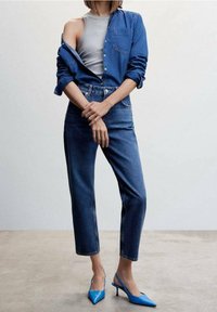 Blauwe denim blouse over een grijze tanktop, gecombineerd met hooggepaste blauwe jeans en puntige blauwe hakken.
