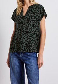 Top corto a maniche corte verde scuro con motivo leopardato, dotato di scollatura a V e una vestibilità comoda, abbinato a jeans blu.