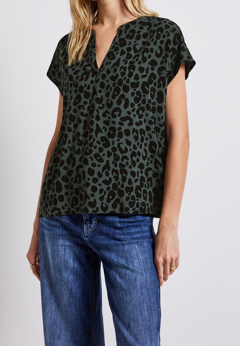 Top corto a maniche corte verde scuro con motivo leopardato, dotato di scollatura a V e una vestibilità comoda, abbinato a jeans blu.