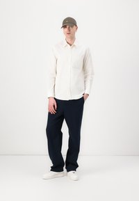 White button-up shirt with a pocket, paired with navy wide-leg pants and white sneakers, topped with a green cap.