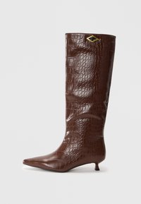 Bottes en cuir marron avec motif crocodile, montantes jusqu'au genou, à bout pointu et petit talon carré. Présente un accent doré en forme de diamant.