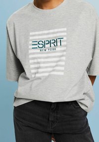 Grå bomull t-shirt med en centralt broderad logotyp med "ESPRIT NEW YORK," accentuerad av vita horisontella ränder. Löst passande design.