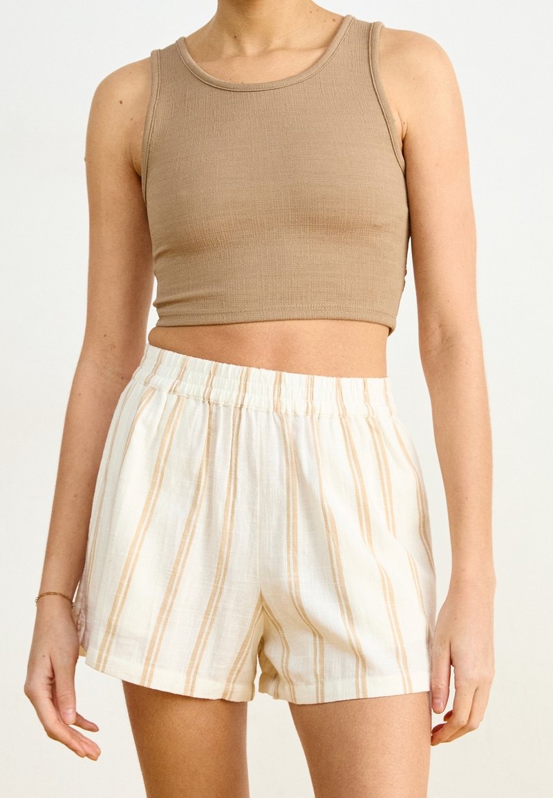 Un crop top côtelé marron associé à un short blanc à rayures verticales beige et à une taille élastique. Texture lisse, design décontracté.