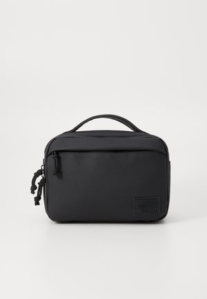 Bolsa rectangular negra hecha de material suave con un asa superior, cremallera frontal y un parche que dice "REUTILIZA RECICLA REPITE."