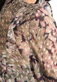 Blusa floreale con design a spalle arricciate, tessuto leggero in beige, rosa e nero con motivi astratti e texture morbida.