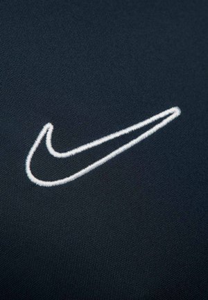 Logo Nike in ricamo bianco su uno sfondo di tessuto scuro e texture, caratterizzato da un design elegante e curvo e una forma distintiva.