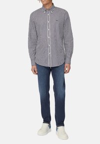 Camicia a righe con colletto, colori blu navy e bianco. Abbinata a jeans in denim scuro e sneakers bianche con accenti blu.