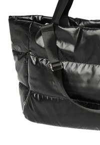 Sac fourre-tout noir matelassé avec une texture brillante et rembourrée ; il dispose de sangles en toile réglables et d'une poche latérale zippée.