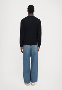 Marineblå strikkegenser med et strukturert bølgemønster, parret med lyseblå vide denimjeans og off-white sneakers.
