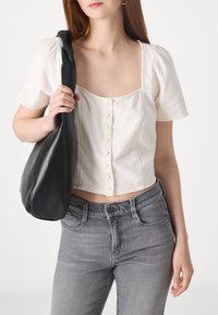 Top bianco corto con maniche a palloncino e dettagli in bottone, abbinato a jeans grigi e una borsa a tracolla in pelle nera.