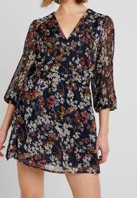 Blommig klänning med marinbakgrund, featuring V-ringning, genomskinliga långa ärmar och elastisk midja, prydd med färgglada blommönster.