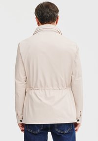 Beżowa kurtka z kołnierzem stójkowym, elastycznym paskiem w talii i mankietami na guziki. Gładka tekstura, minimalistyczny design i klasyczny krój.