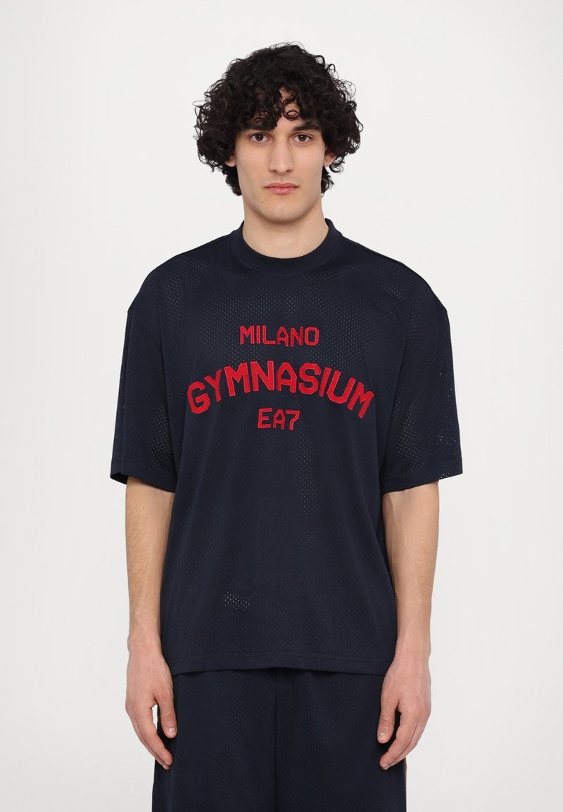Jūras spēku acs sporta t-krekls ar sarkanu izšūtu tekstu "MILANO GYMNASIUM EA7". Brīvs piegriezums ar īsām piedurknēm un apaļu kakla izgriezumu.