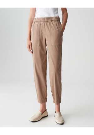 Lichtbruin stretchbroek met elastische tailleband, twee voorzakken, taps toelopende pijpen en een gladde textuur, gecombineerd met beige instapschoenen.