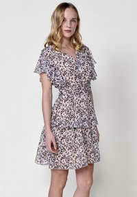 Kleid aus leichtem Stoff mit Blumenmuster, ausgestattet mit Rüschärmel und einem gestuften Design. Die Farben umfassen sanftes Rosa, Beige und dunkle Flecken.
