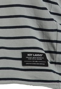 Tela a rayas en gris claro con líneas azul marino oscuras. Presenta una etiqueta clave con el logotipo y texto, enfatizando la marca y la calidad.