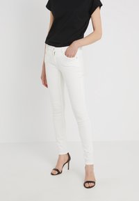 Vita slim-fit jeans med en slät yta, som har dragkedja och framfickor. Kombinerat med en svart t-shirt med korta ärmar och svarta klackar.