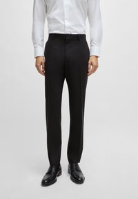 Sorte skreddersydde bukser med en jevn stoff, rette passform og minimalistisk design, kombinert med en hvit skjorte med knapper og svarte sko.
