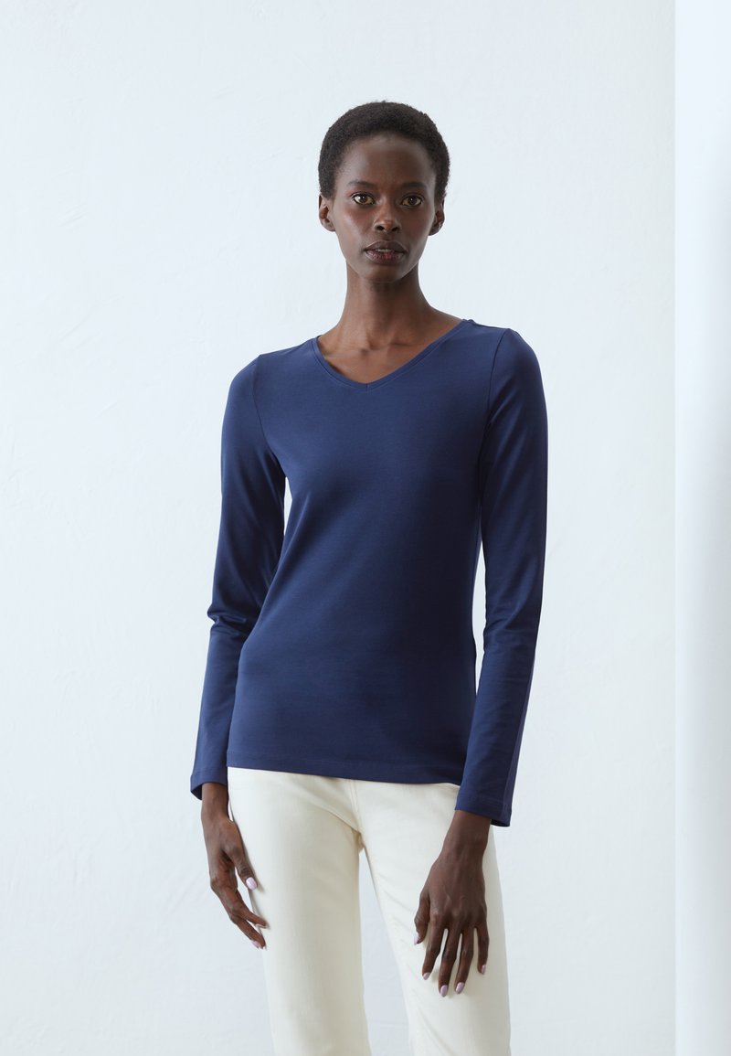 Maglietta a maniche lunghe blu navy con scollatura a V, realizzata in un tessuto liscio, abbinata a pantaloni chiari. Design minimalista, senza motivi.