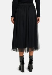 Gonna midi in tulle nera con vita elastica arricciata e design a strati. Indossata con stivaletti a zeppa neri lucidi.