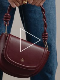 Bordo spalvos odinė rankinė su išlenkta rankena, auksinės spalvos furnitūra ir užsegimas su subtiliu siuvinėjimu bei logotipo detalėmis.