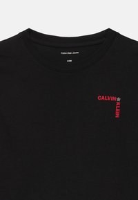 Černé tričko s kulatým výstřihem, na levé části hrudi malý červený nápis "CALVIN KLEIN" a šedá hvězda, velikost 8 (128).