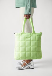 Jastučićasta torba u svijetloj limetastoj zelenoj boji s quilted dizajnom, čvrstim ručkama i zatvaračem na vrhu. U kombinaciji sa srebrnim Mary Jane cipelama.