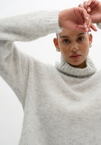 Light gray knitted sweater with a high, ribbed collar and relaxed fit. Soft texture with visible horizontal stripes and rolled cuffs.