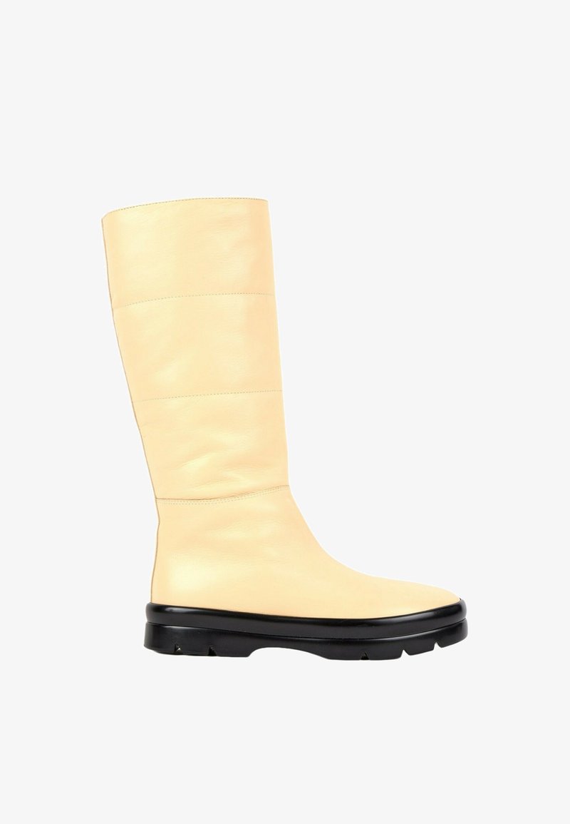 Botte en cuir couleur crème montant jusqu'au genou, avec un bout arrondi et une semelle épaisse en caoutchouc noir avec crampons pour l'adhérence.