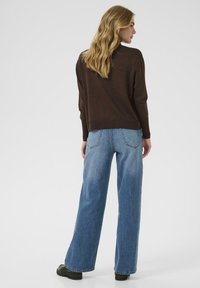 Brązowy sweter dzianinowy zestawiony z jasnoniebieskimi spodniami typu wide-leg z wysokim stanem. Spodnie mają tylne kieszenie i klasyczną fakturę jeansu.