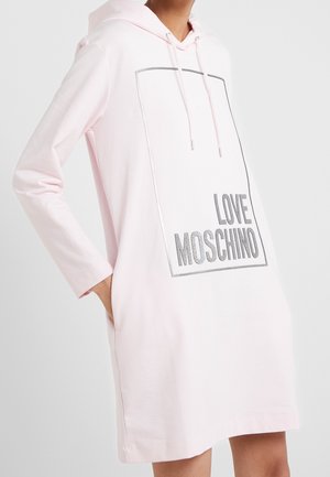Persoon die een lichtroze hoodiejurk met lange mouwen draagt en tekst "LOVE MOSCHINO" binnen een rechthoekige omlijning aan de voorkant.