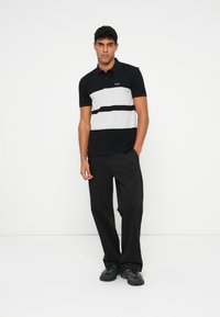Black and gray striped polo shirt with short sleeves, featuring a logo on the chest, paired with loose-fitting black trousers and black shoes.