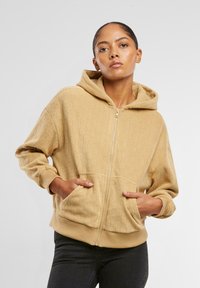 Hanorac crem cu glugă, cu fermoar, având un model texturat în romburi, buzunare tip kangaroo și mansete cu striatii, destinat pentru purtare casual.
