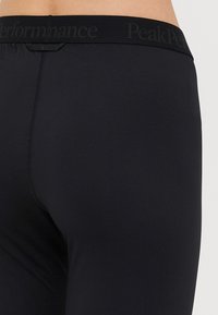 Leggings pretos com um tecido suave e elástico. A cintura apresenta um discreto logótipo da Peak Performance em preto. Sem padrões ou acentos visíveis.