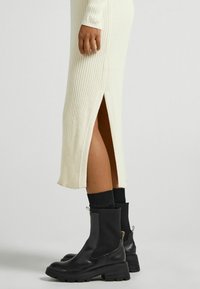 Svarta anklarstövlar med en kraftig sula, elastiska sidopaneler och dragremmar, i kombo med en krämfärgad ribbad stickad klänning med en sidoklyfta.